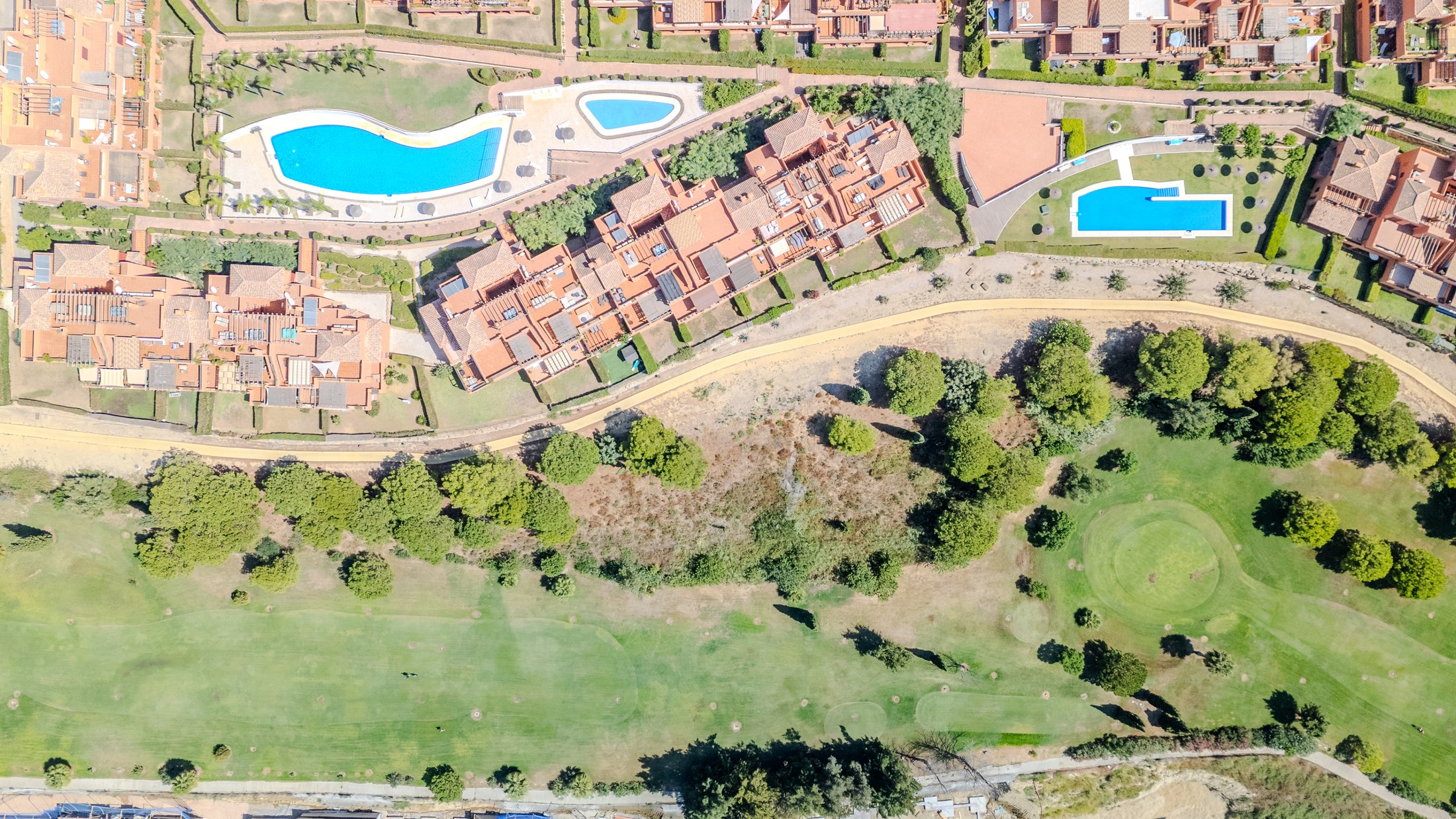 Overhead view of terracotta homes, communal pools and gardens beside the golf course