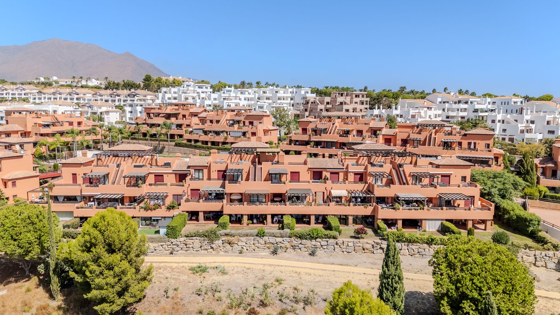 Terracotta homes, mature greenery and mountains seen from above Casares Golf Gardens